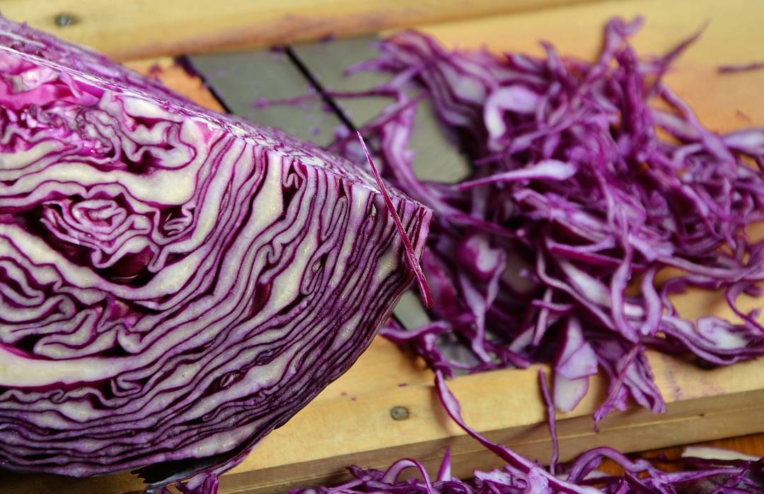 Close-up of sliced red cabbage with shredded pieces on a wooden cutting board, illustrating Red Acre seeds variety.