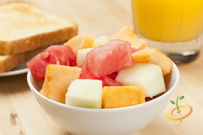 Bowl of mixed melon fruit including honeydew, orange flesh melon, and watermelon with toast and glass of orange juice in background