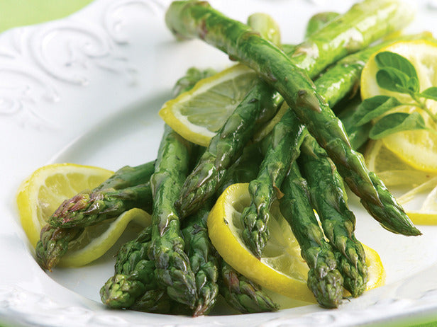 Fresh asparagus spears with lemon slices on a white background, showcasing Mary Washington asparagus seeds from SeedsNow.